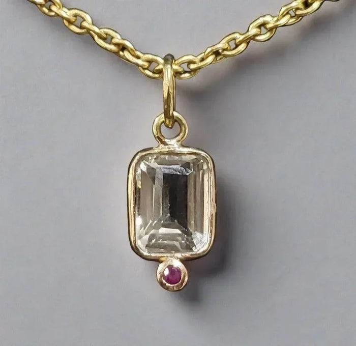 Elegant gold necklace with emerald-cut gemstone pendant and ruby accent, showcasing fine jewelry craftsmanship