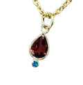 Elegant gold necklace with teardrop garnet pendant and blue gem accent, perfect for sophisticated jewelry lovers