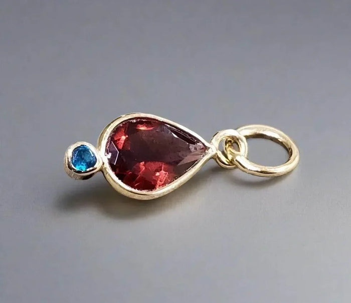 Gold pendant with red teardrop gem and blue accent stone, elegant jewelry accessory