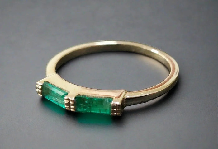 Elegant gold ring with two vibrant emerald gemstones, showcasing timeless sophistication and luxury.
