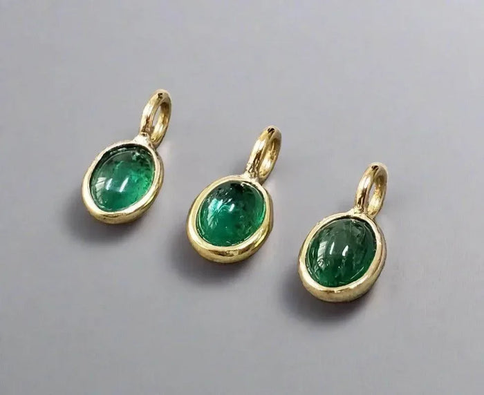 Three gold pendants with oval emerald gemstones, elegant jewelry accessories