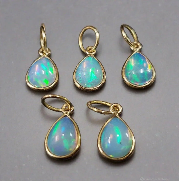 Five teardrop opal pendants in gold settings, showcasing vibrant blue and green fire