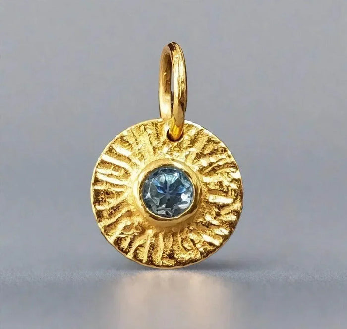 Gold pendant with textured sunburst design and blue gemstone, elegant jewelry accessory