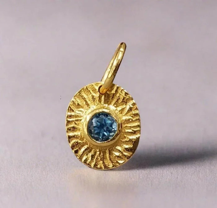 Gold pendant with blue gemstone, textured sunburst design, elegant jewelry accessory