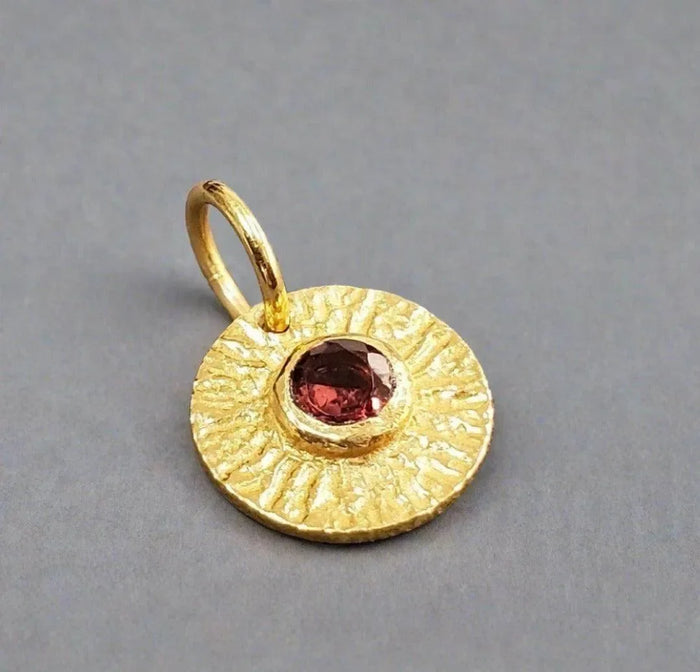 Gold pendant with textured sunburst design and red gemstone, elegant jewelry accessory