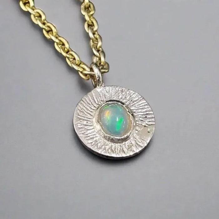 Elegant opal pendant necklace with textured silver setting and gold chain, perfect for sophisticated jewelry lovers