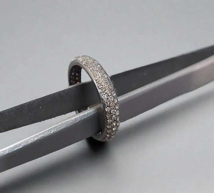 Elegant diamond pavé ring held by tweezers, showcasing sparkling brilliance and fine craftsmanship.
