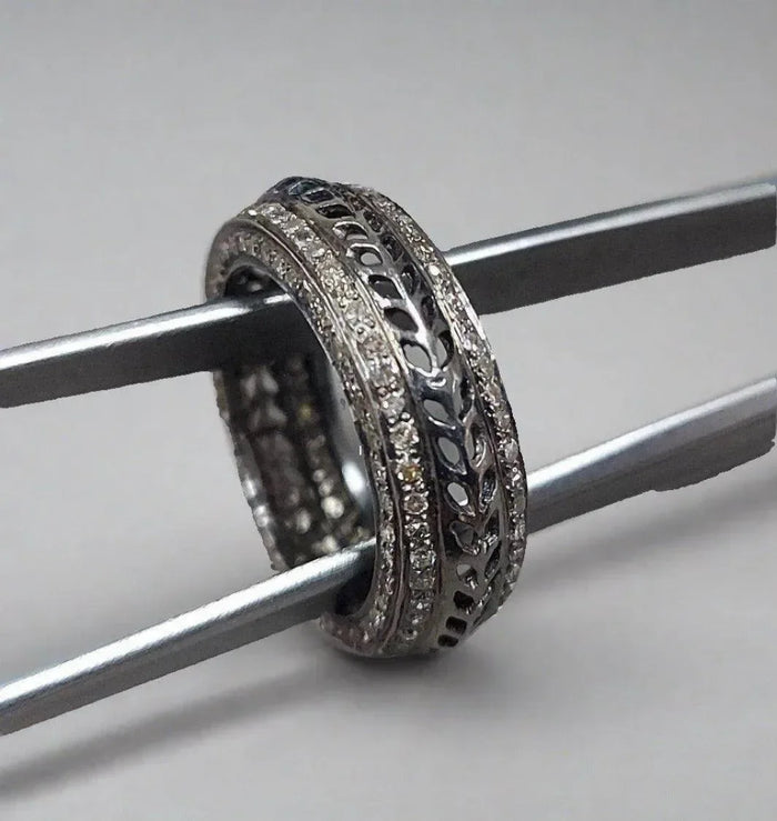 Elegant diamond-encrusted filigree ring held by tweezers, showcasing intricate craftsmanship and sparkle.