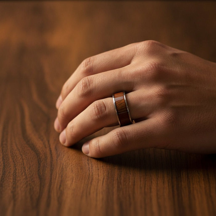 BOKKEN flat silver tungsten wedding band with black walnut wood inlay running around the band and polished silver edges worn on man's hand resting on walnut wood, lifestyle photo