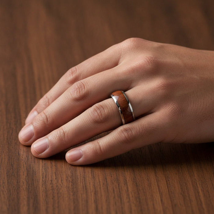 DALBERG silver tungsten carbide domed wedding band with rosewood inlay running around the band and polished finish worn on man's hand resting on walnut wood, lifestyle photo