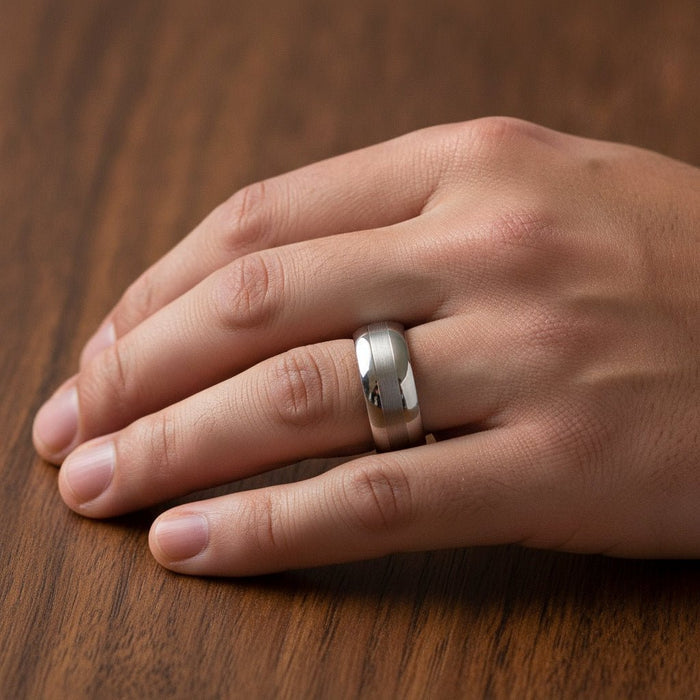 DEFIANCE silver tungsten domed wedding band with a single brushed vertical stripe running around the center and polished sides worn on man's hand resting on walnut wood, lifestyle photo