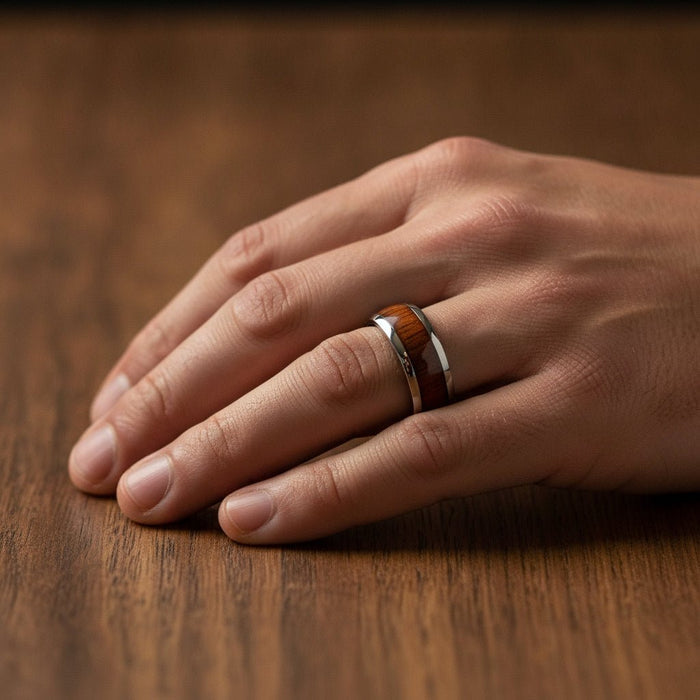 KAMEHA silver tungsten domed wedding band with koa wood inlay running around the band and polished finish worn on man's hand resting on walnut wood, lifestyle photo