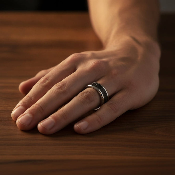 KILAUEA polished silver tungsten wedding band with black and gray lava rock stone inlay running around the band and polished beveled edges worn on man's hand resting on walnut wood, lifestyle photo