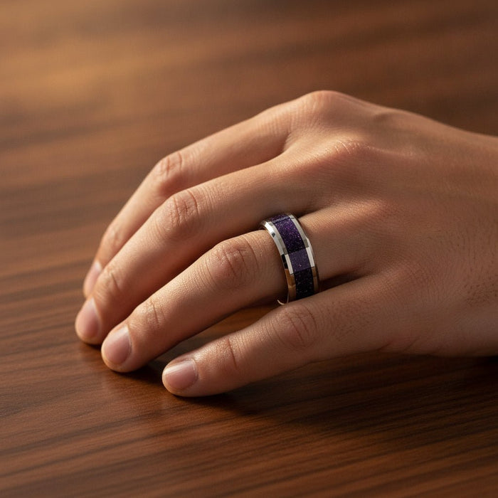 MAKI polished silver tungsten wedding band with sparkling purple goldstone inlay running around the band and polished beveled edges worn on man's hand resting on walnut wood, lifestyle photo