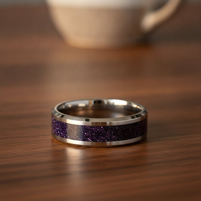 MAKI polished silver tungsten wedding band with sparkling purple goldstone inlay running around the band and polished beveled edges resting on a walnut wood counter, lifestyle scene