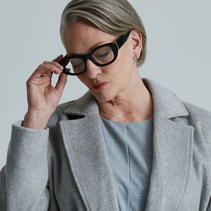 lifestyle - business suited female looking down wearing the devil wears prada x diff eyewear featuring the miranda square oversized prescription glasses with a black acetate frame angled view