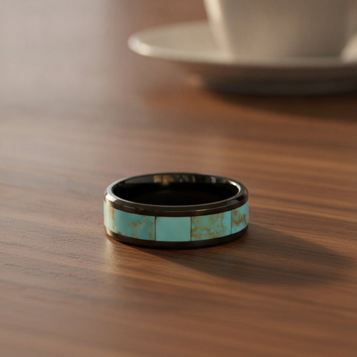 PIETRO polished black ceramic wedding band with light blue turquoise stone inlay running around the band and polished beveled edges resting on a walnut wood counter, lifestyle scene