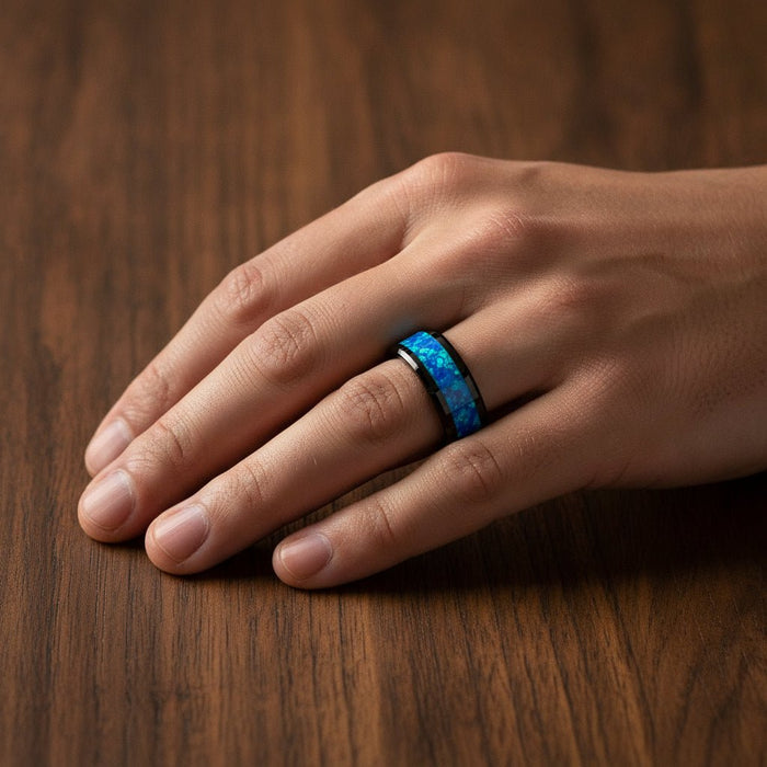 QUANTUM black ceramic wedding band with blue and green opal inlay running around the band and polished beveled edges worn on man's hand resting on walnut wood, lifestyle photo