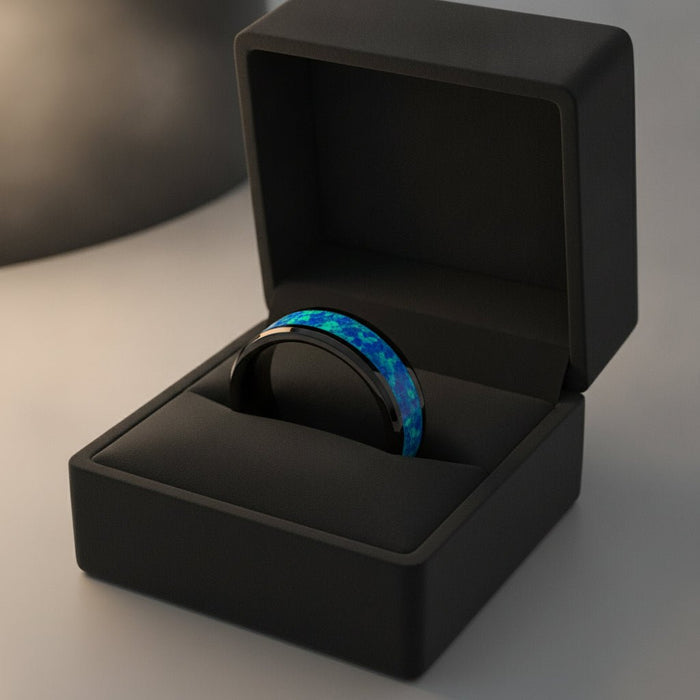 QUANTUM black ceramic wedding band with blue and green opal inlay running around the band and polished beveled edges nested in a black velvet ring box, editorial jewelry shot
