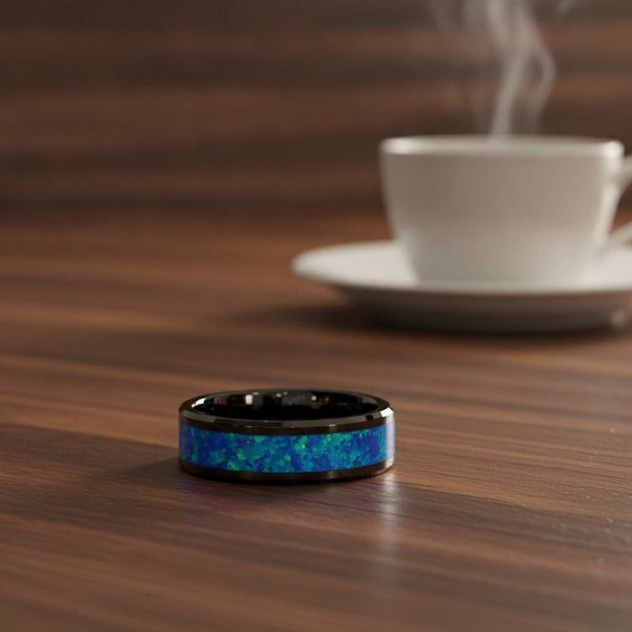 QUANTUM black ceramic wedding band with blue and green opal inlay running around the band and polished beveled edges resting on a walnut wood counter, lifestyle scene