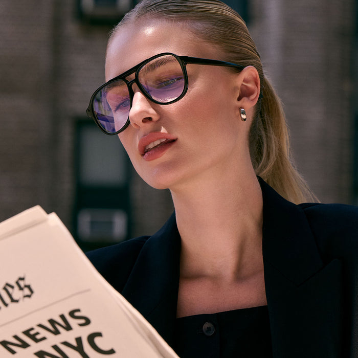 on model - female reading the newspaper while wearing diff eyewear featuring the tatum aviator prescription glasses with a black frame angled view