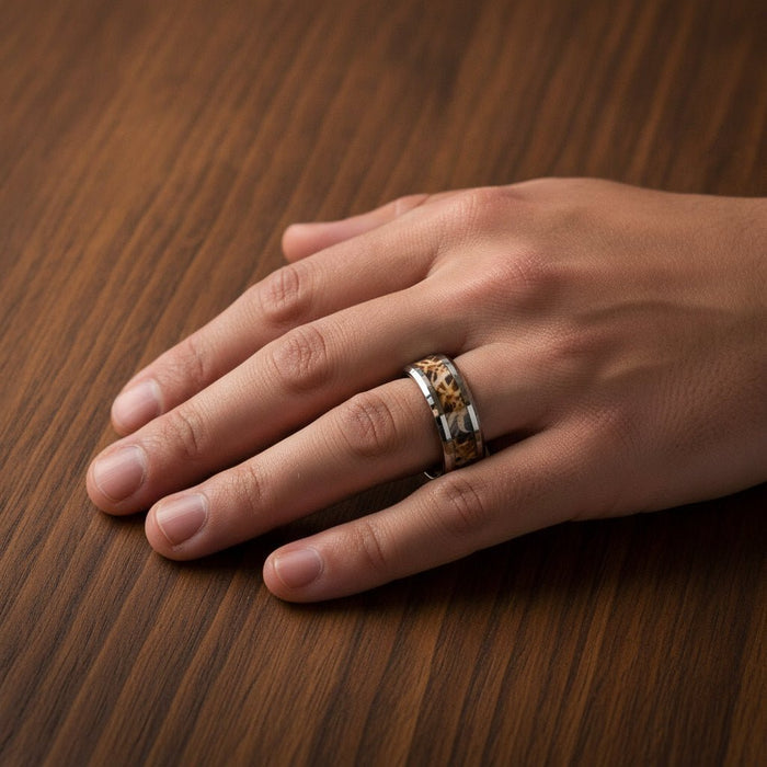 TERRA silver tungsten carbide wedding band with leaves and grassland woodland camouflage inlay running around the band and polished edges worn on man's hand resting on walnut wood, lifestyle photo