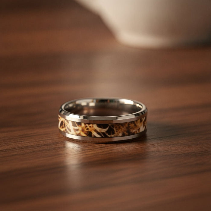 TERRA silver tungsten carbide wedding band with leaves and grassland woodland camouflage inlay running around the band and polished edges resting on a walnut wood counter, lifestyle scene