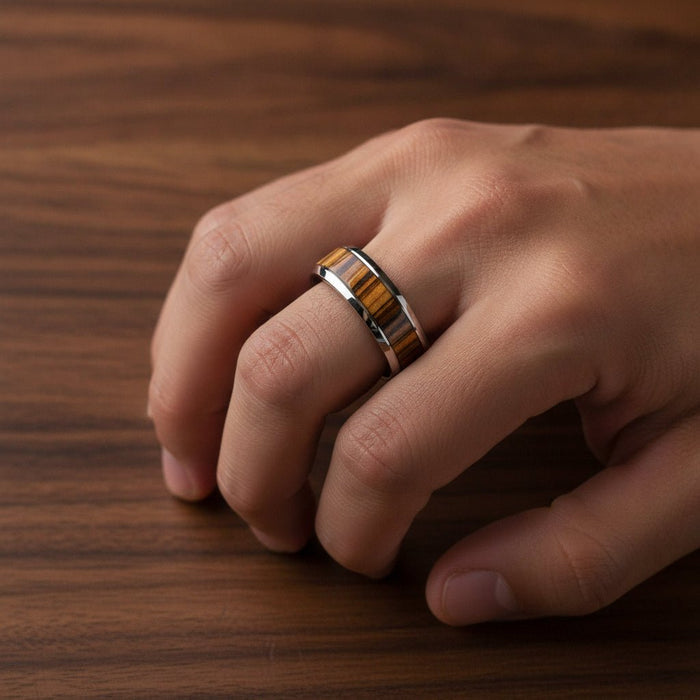TIGRE silver tungsten wedding band with striped zebra wood inlay running around the band and polished edges worn on man's hand resting on walnut wood, lifestyle photo