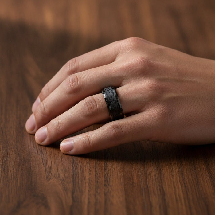 VESUVIUS polished black ceramic wedding band with black and gray lava rock stone inlay running around the band and polished beveled edges worn on man's hand resting on walnut wood, lifestyle photo