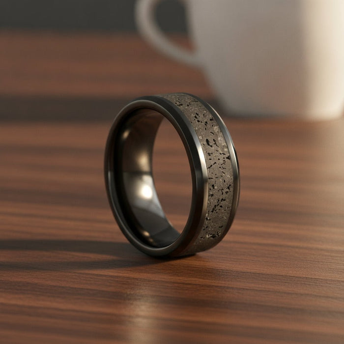 VESUVIUS polished black ceramic wedding band with black and gray lava rock stone inlay running around the band and polished beveled edges resting on a walnut wood counter, lifestyle scene